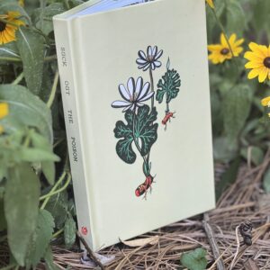 A cream-colored hardcover journal with a bloodroot illustration on the cover and "suck out the poison" on the spine sits in a patch of brown-eyed susans
